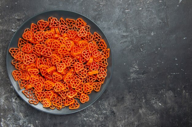 Top view heart shaped italian pasta on black plate on dark table copy space