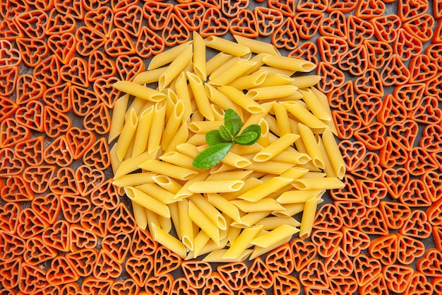 Top view heart shaped italian pasta and penne on dark table