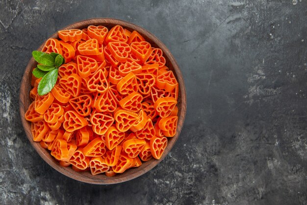 Top view heart shaped red italian pasta in a bowl on dark table with free space