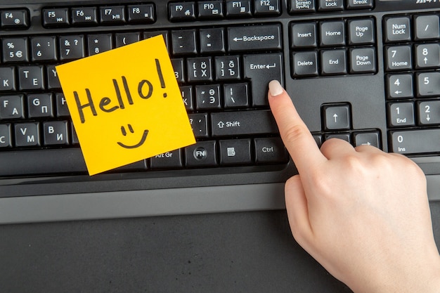 Top view hello written on note paper female hand on keyboard at enter key on dark background