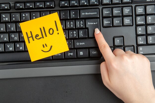 Top view hello written on note paper female hand on keyboard at enter key on dark background