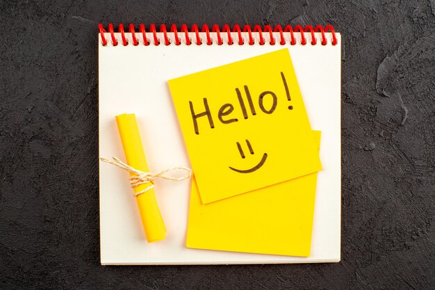 Top view hello written on sticky note on notepad rolled up note tied with rope on black table