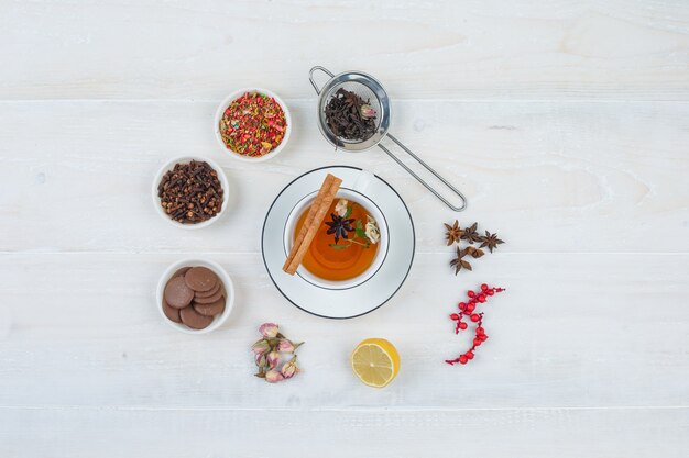 Top view herbal tea and cookies with tea strainer,herbs and spices on white surface