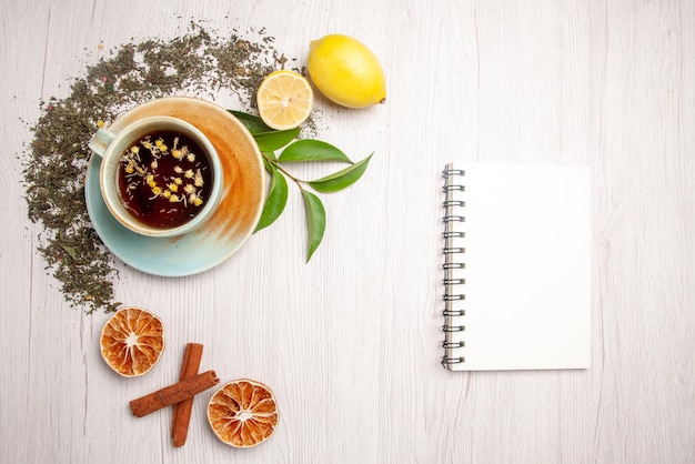 Top view herbal tea white cup of herbal tea next to the white notebook herbs lemon cinnamon on the white table