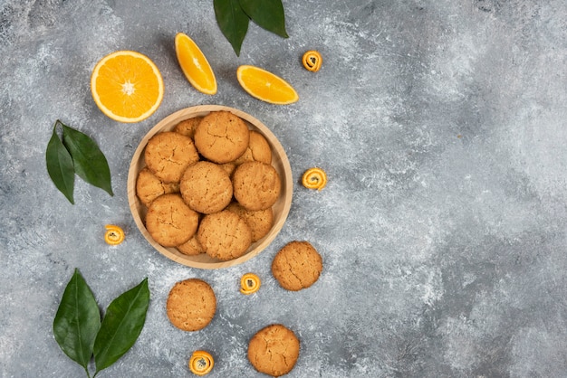 Top view of homemade cookies on wooden board and oranges with leaves over grey surface. High quality illustration