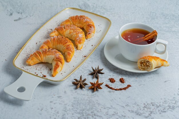 Top view of homemade fresh croissants with fresh tea on grey surface.