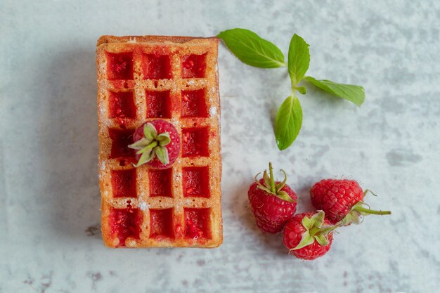 Top view of homemade waffles with raspberry jam on grey surface. 