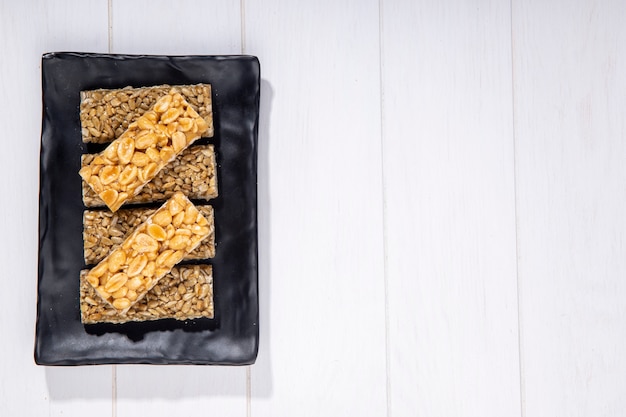 Top view of honey bars with peanuts and sunflower seeds on a black platter with copy space on rustic