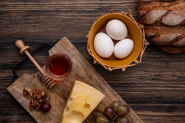 木製の背景に鶏卵と黒パンとスタンドにチーズとクルミと瓶の中の蜂蜜の上面図