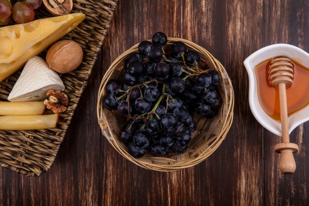 Top view honey in a saucer with grapes  varieties of cheeses and nuts on a stand on a wooden background