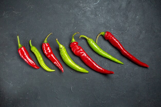 Top view horizontal row green and red peppers on dark surface with free place