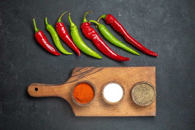 Top view horizontal row green and red peppers different spices on cutting board on dark surface