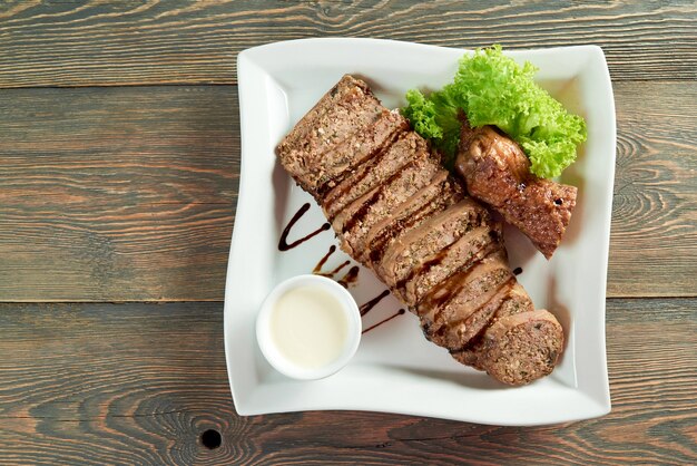 装飾された食品レシピディナーディナーランチディナーディナーローストソースグリーンを食べる木製のテーブルcopyspaceの白い正方形のプレートにスライスした肉の平面図水平ショット。