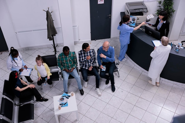 Foto gratuita vista dall'alto della reception dell'ospedale gruppo eterogeneo di persone in attesa del prossimo appuntamento dal medico mentre parlano di problemi medici. infermiera professionista che controlla appuntamento per madre e bambino.