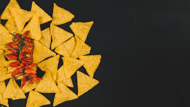 Top view of hot mexican nachos chips with red chilies over black backdrop