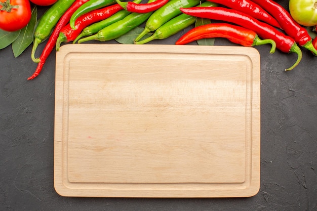 Top view hot red and green peppers and tomatoes bay leaves and a chopping board on black ground