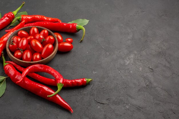 Top view hot red peppers and bay leaves and a bowl of cherry tomatoes at the left side of the black table with copy space