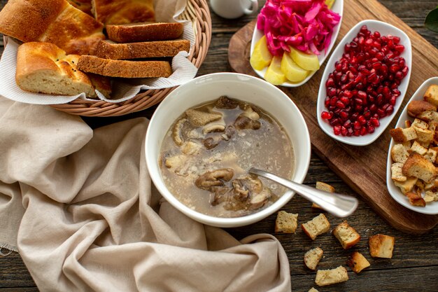 A top view hot soup along with bread slcies pomegranate peeled out and fresh vegetables on the brown wooden rustic floor