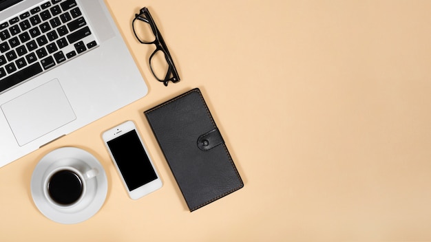 Free photo top view of hot tea; mobile phone; eye glasses; diary and laptop over beige background