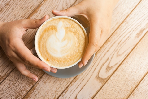 Top view of human hand holding latte coffee cup over wooden surface