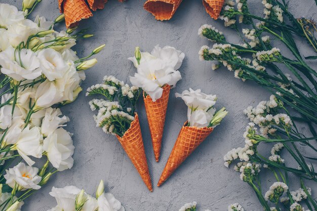 Top view of ice cream cones with flowers on light gray