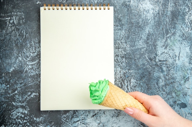 Top view ice cream in woman hand a notebook on dark surface