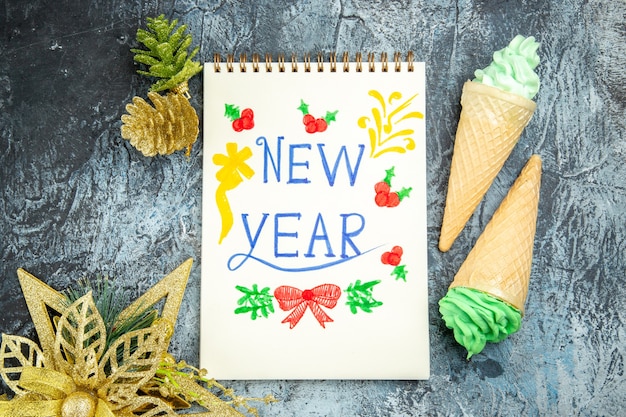Top view ice creams new year written on notebook xmas ornaments on grey background