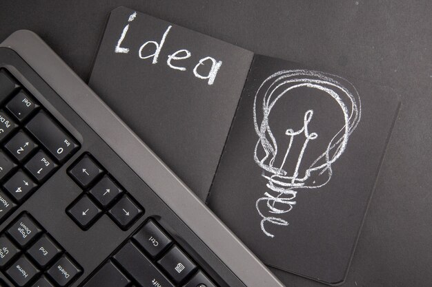 Top view idealight bulb drawing on black notepad keyboard on dark