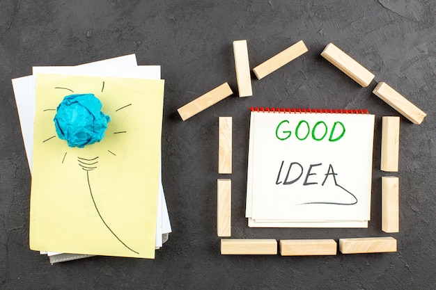 Idea vista dall'alto lampadina su blocchi di legno a forma di casa di carta buona idea scritta su taccuino sul tavolo nero