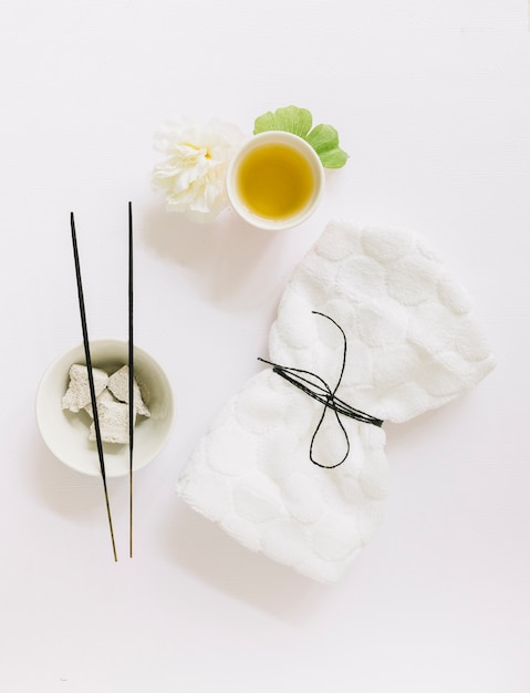 Top view of incense stick; pumice stone; flower; gingko leaf; oil and tied napkin on white background