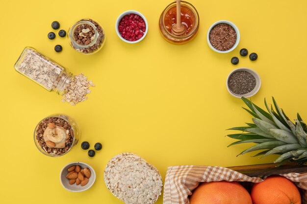 Top view of ingredients for making snack as oat walnut crispbread jam red currant almond blackthorn with smoothie pineapple leaves and citrus fruits on yellow background