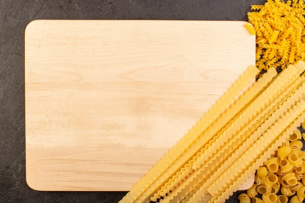 A top view italian dry pasta yellow raw along with square formed cream colored desk isolated on the dark