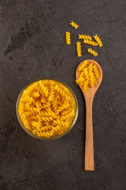 A top view italian dry pasta yellow raw inside bowl with spoon isolated on the dark