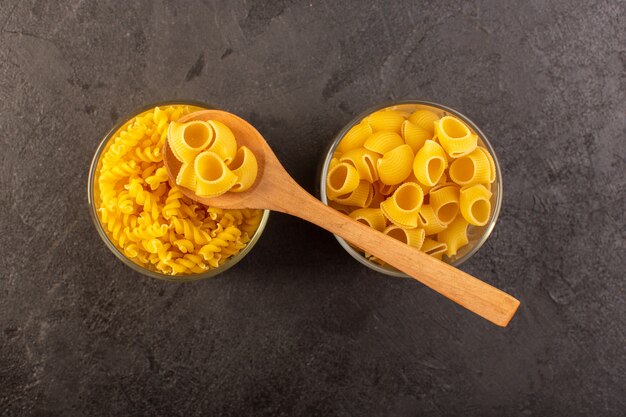 A top view italian dry pasta yellow raw inside bowls with spoon isolated on the dark