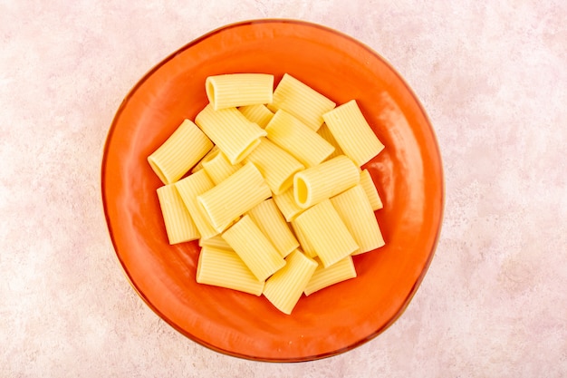 Итальянская паста, вид сверху, вкусная и соленая на круглой оранжевой тарелке на розовом столе