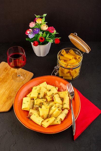 상위 뷰 이탈리아 파스타는 디자인 된 카펫과 어두운 책상에 담근 꽃과 함께 둥근 주황색 접시 안에 맛있는 소금에 절인 요리