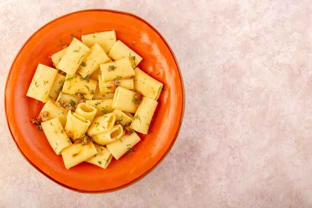 상위 뷰 이탈리아 파스타는 말린 채소로 맛있게 요리하고 분홍색 책상에 둥근 주황색 접시 안에 소금에 절인 것입니다.
