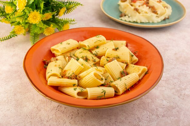 上面図イタリアンパスタは乾燥した緑とおいしい調理し、ピンクの机の上の花と丸いオレンジプレートの内側に塩漬け