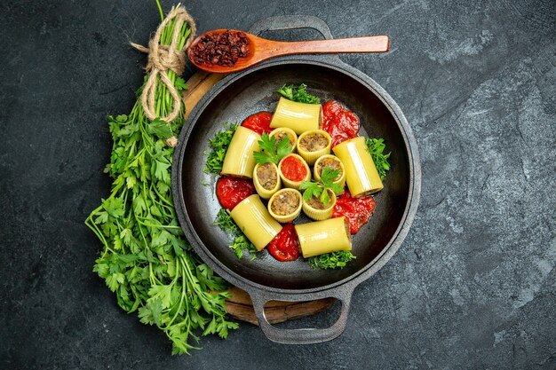 Вид сверху итальянская паста с зеленью, томатным соусом и мясом внутри сковороды на сером пространстве