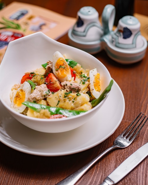 Top view of italian potato salad bowl with tuna beans cherry tomato parsley boiled eggs and olive oil