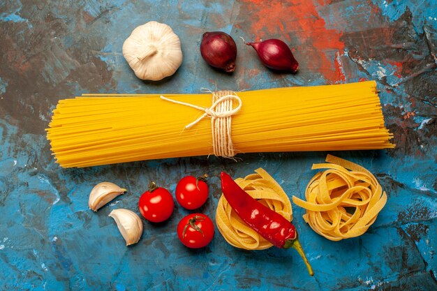夕食の準備のためのイタリアの様々なパスタの上面図青背景にニンニクピーマントマト玉ねぎ