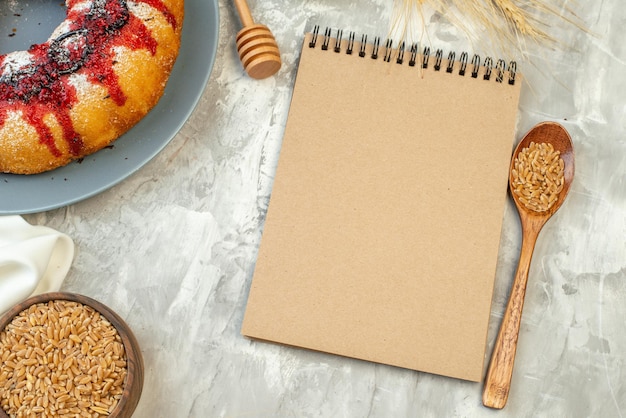 Free photo top view jam cake on round plate wheat grains in bowl and wooden spoon notebook on table