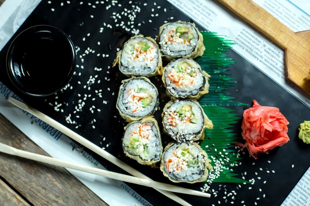 Вид сверху японской традиционной еды темпура суши маки подается с имбирем и соевым соусом на черной доске