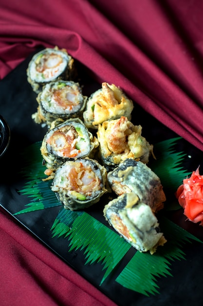 Top view of japanese traditional food tempura sushi maki served with ginger and soy sauce on a black board