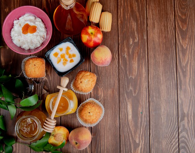 Top view of jars of jams as peach and plum with cupcakes peaches cottage cheese on wooden surface decorated with leaves with copy space