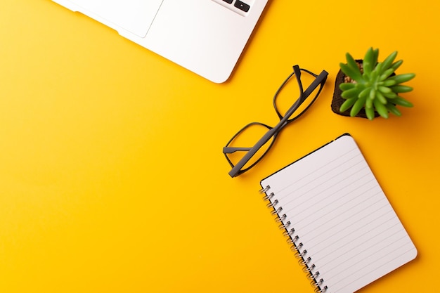 Top view of a journal, a laptop, glasses, and a plant isolated on a yellow background