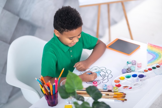 Top view of joyful boy drawing with crayons