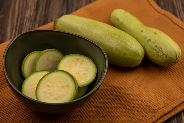 Free photo top view of juicy chopped zucchinis on a bowl with zucchinis isolated on a cloth on a wooden wall