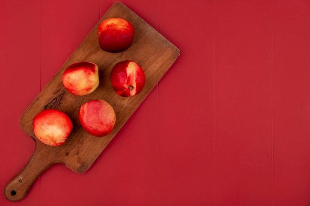 Free photo top view of juicy and delicious peaches on a wooden kitchen board on a red background with copy space