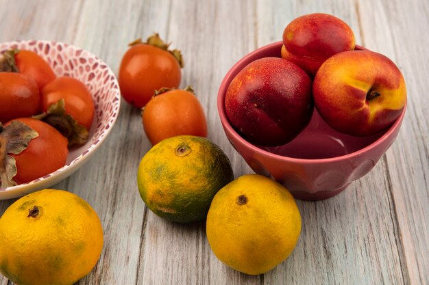 Top view of juicy soft peaches on a bowl with persimmons and tangerines isolated on a grey wooden wall